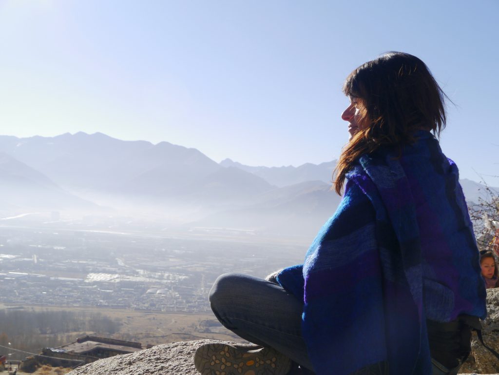 Viajar bien no es cuestión de suerte (es cuestión de cómo te montas el viaje) Yaiza sentada frente al paisaje montañoso del Tíbet, en el Himalaya.