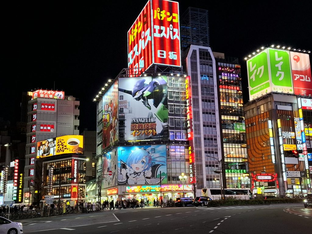Vista nocturna de una avenida iluminada en Shinjuku, Tokio, con pantallas