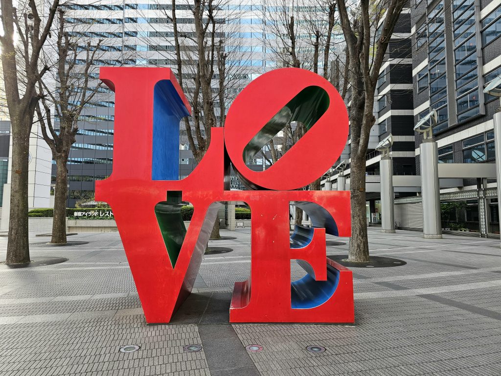 Escultura roja LOVE en una plaza de Shinjuku rodeada de rascacielos y árboles.