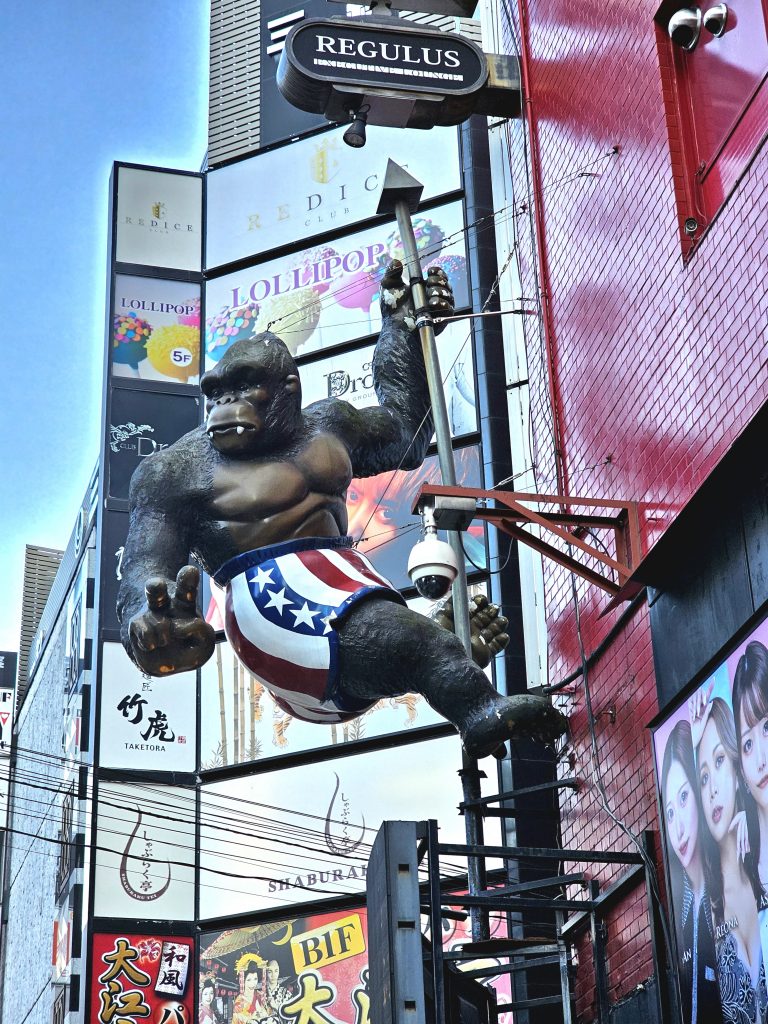 Figura decorativa de un gorila colgada en una fachada de Shinjuku rodeada de carteles y edificios.